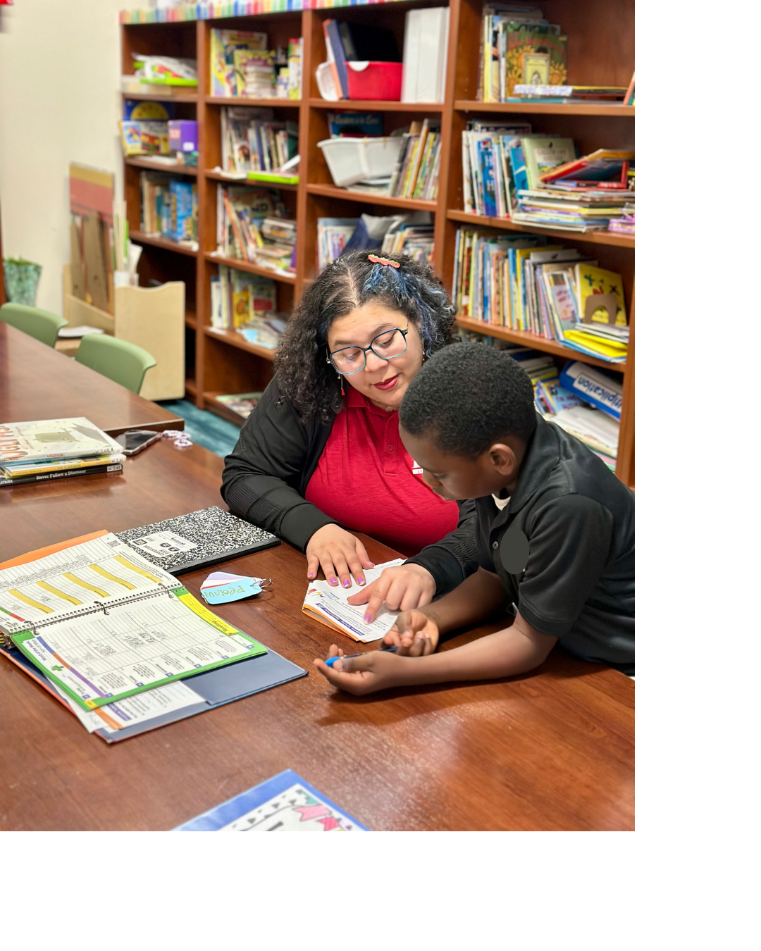 Americorps serice member reading to a student, both sitting at a table